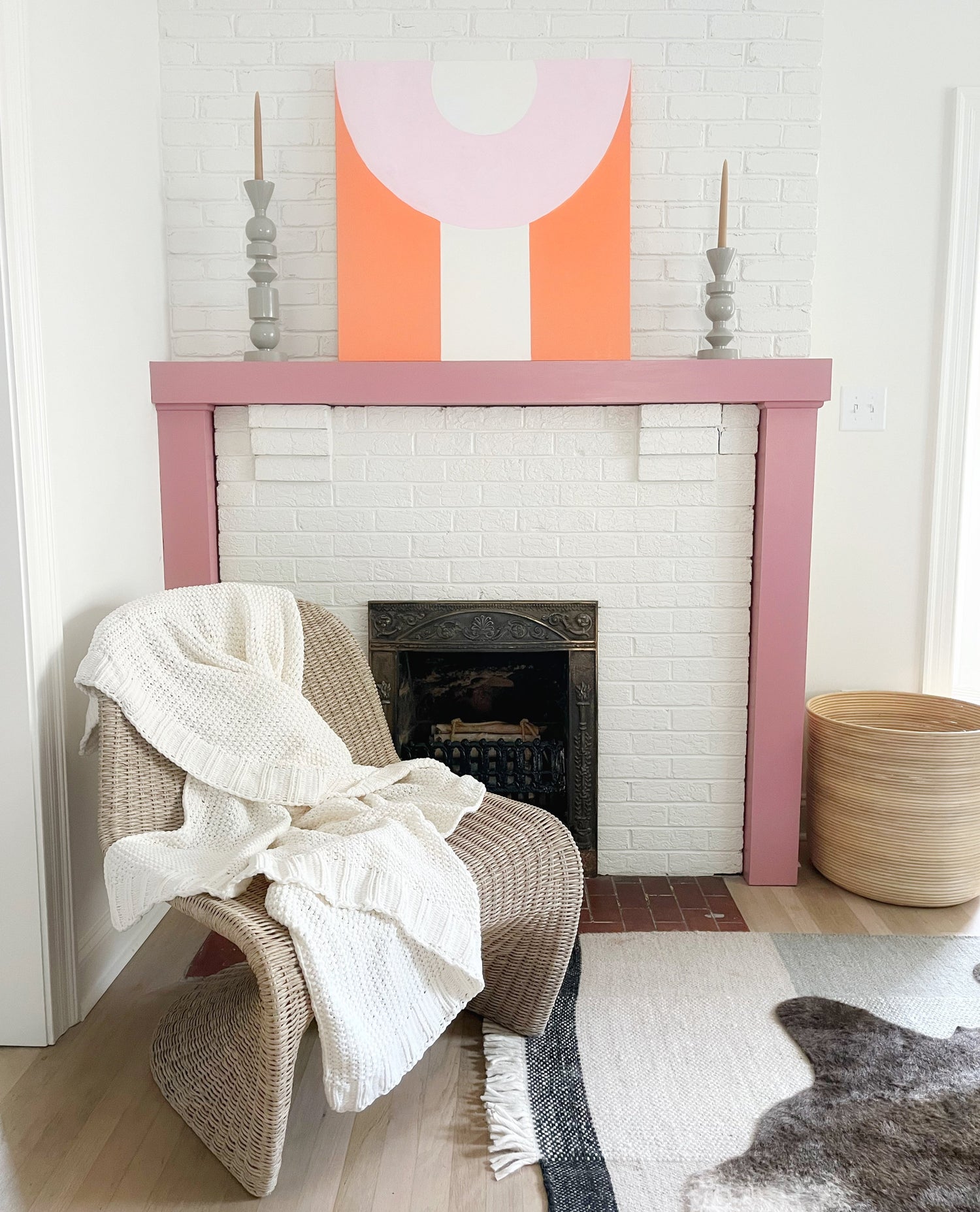 Living room with a white brick fireplace, wicker chair, abstract painting, and decorative items.